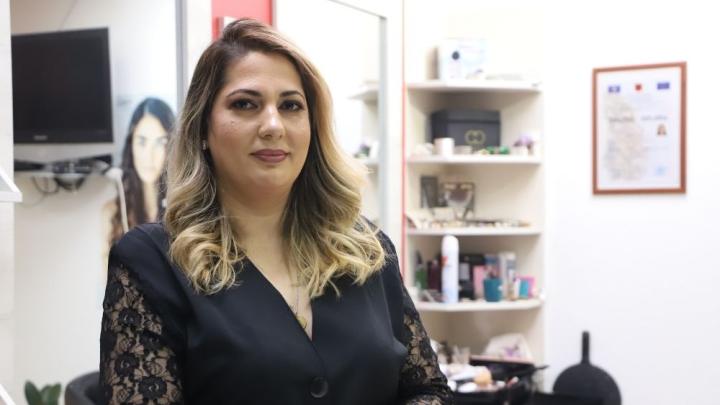   A woman stands in a hairdressing salon and looks into the camera. 