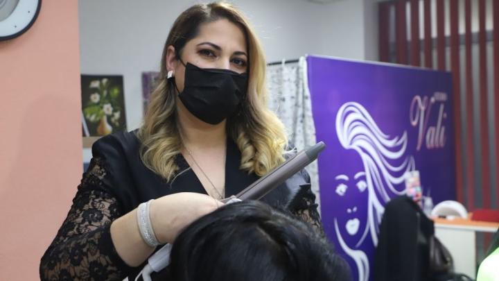  A hairdresser is working on a customer's hair with an electric curling iron. 